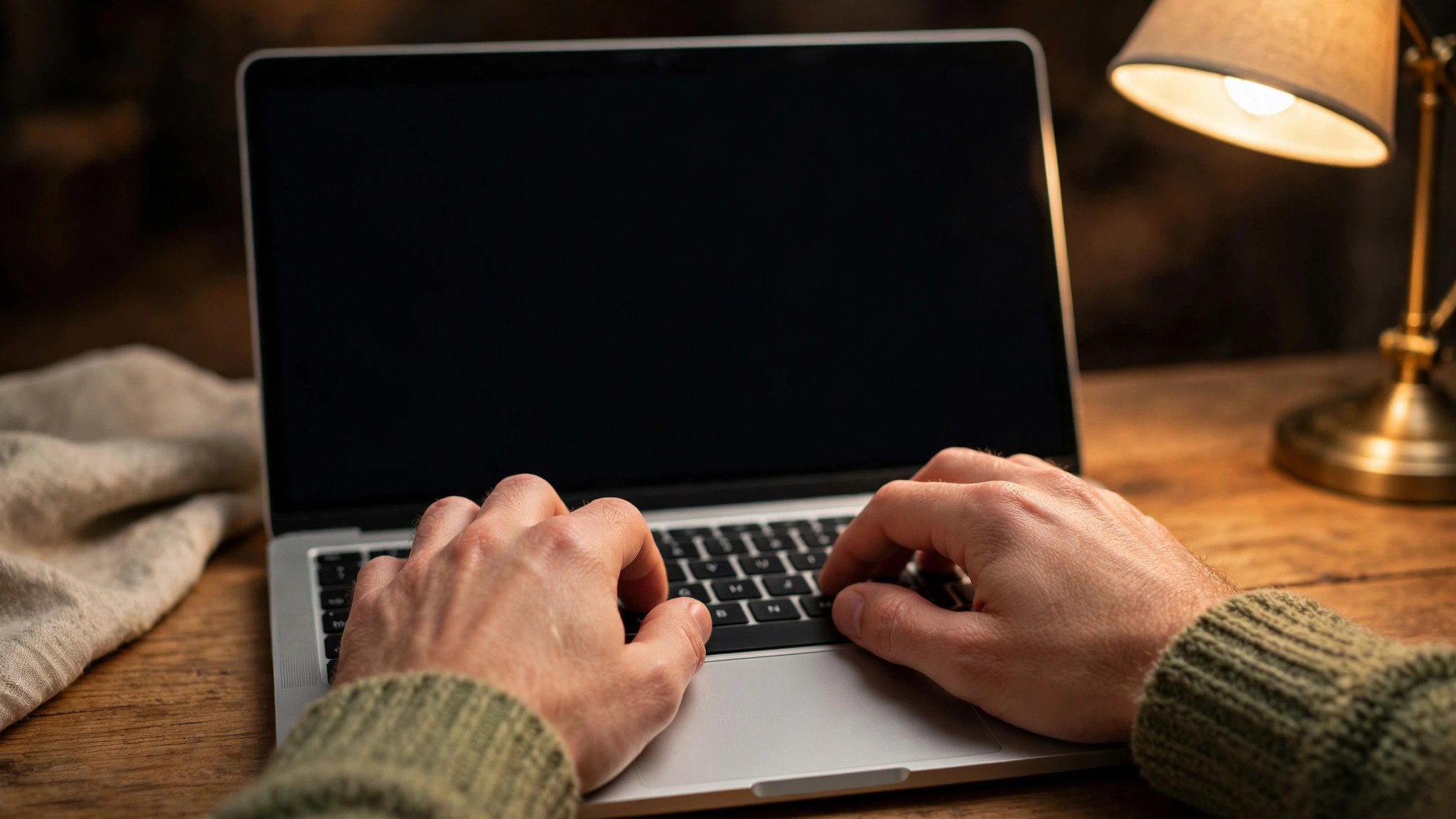 Hands typing on laptop, blank screen, warm desk lamp